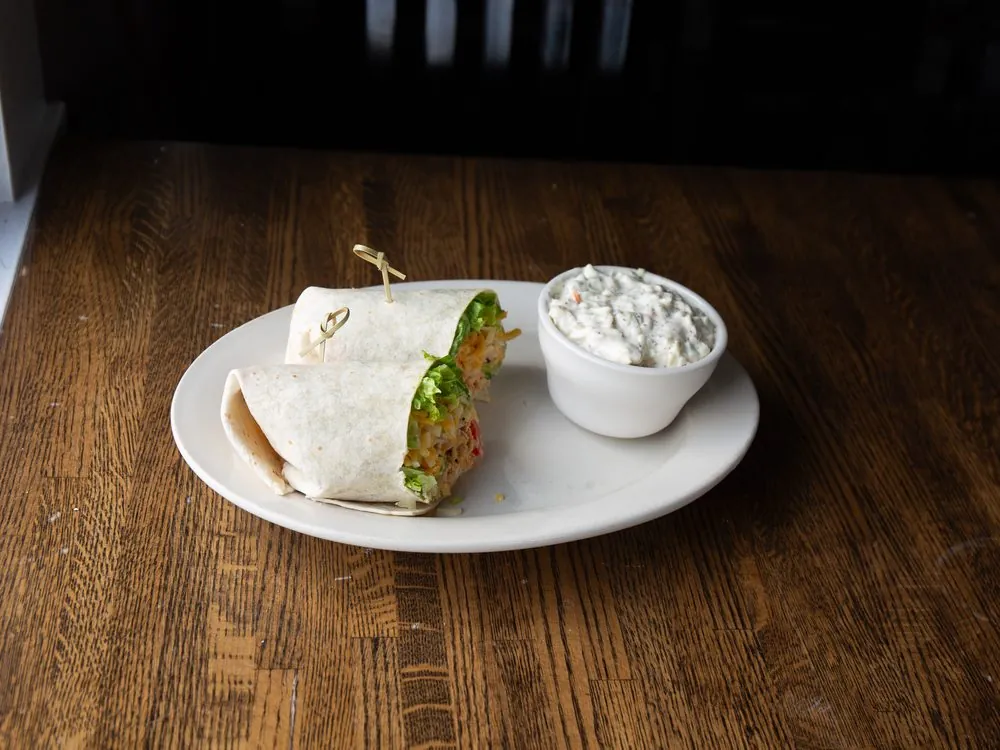 A chicken wrap and dip on a wood table in window light