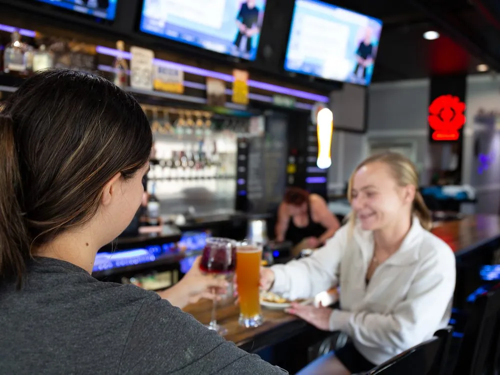 Two friends laughing over a glass of wine and a beer at the bar