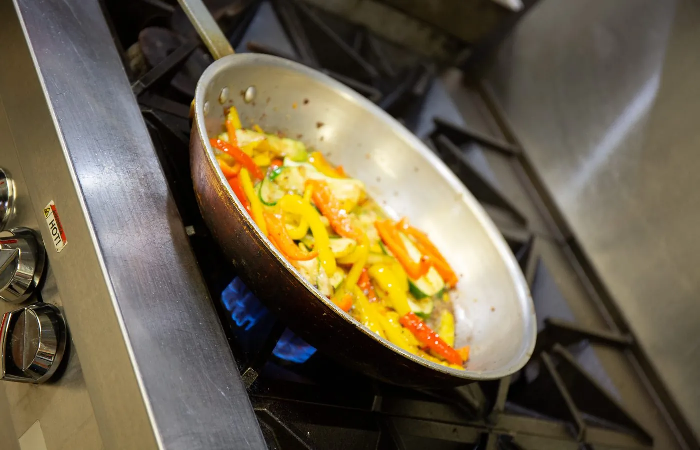 Fresh peppers and zucchini in a sauté pan over an open flame in the kitchen